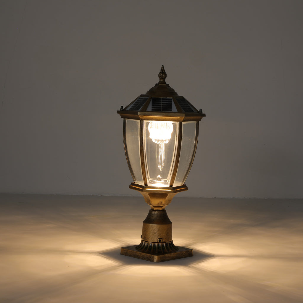 Antique gold solar post cap light lit with a warm glow, showing the hexagonal lantern, clear glass panels, solar cap and fluted metal base