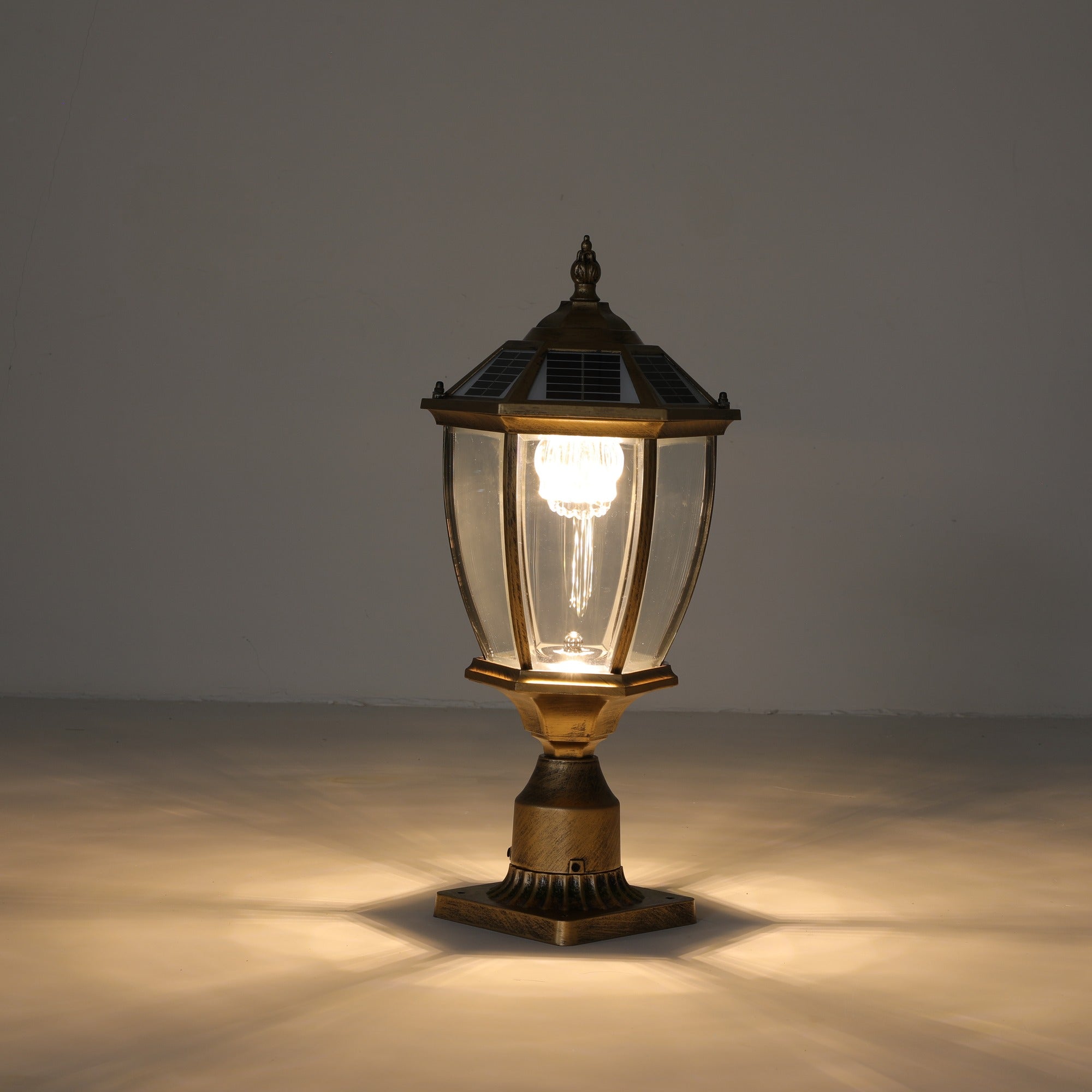 Antique gold solar post cap light lit with a warm glow, showing the hexagonal lantern, clear glass panels, solar cap and fluted metal base