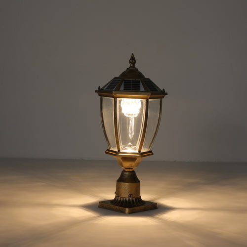 Antique gold solar post cap light lit with a warm glow, showing the hexagonal lantern, clear glass panels, solar cap and fluted metal base